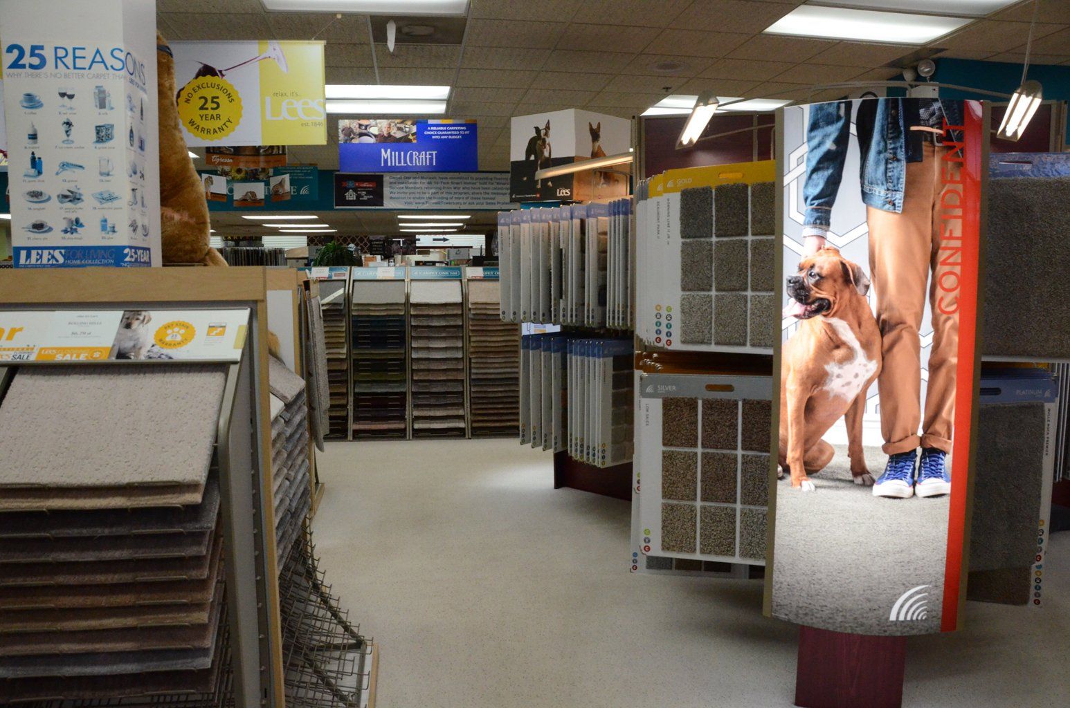 A store aisle with carpet samples, display racks, and a blue sign in a brightly lit showroom.