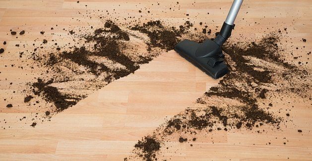 Vacuum cleaner head sweeping dirt off a hardwood floor, with scattered soil around it
