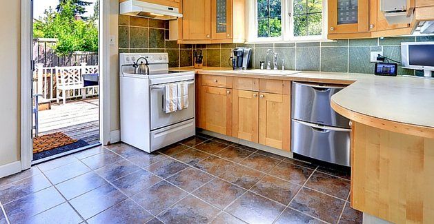 Bright kitchen with wood cabinets, gray tile floor, stainless appliances, and an open door to a patio.