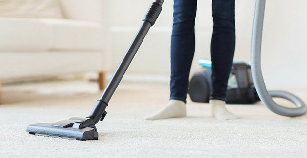 Vacuum cleaner nozzle cleaning a carpet beside a person's legs in a bright living room