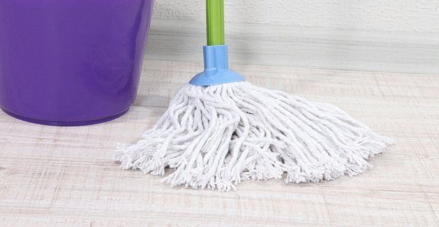 White mop head on a light wood floor beside a purple bucket