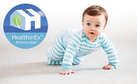 Baby crawling on white floor beside HealthinEx Antimicrobial logo
