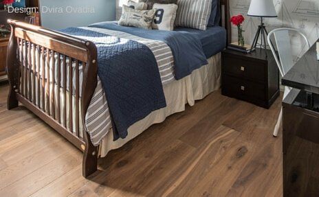 Bedroom with wooden bed frame, blue quilt, gray rug, and bedside table beside a chair by the window