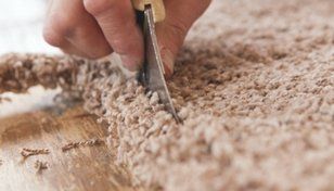Hand cutting a beige carpet with a utility knife