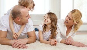 Family lying on a carpet, smiling and talking together in a bright living room