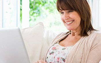 Smiling woman using a laptop on a white couch in a bright room