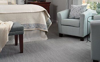 Cozy bedroom seating area with a light blue armchair, upholstered bench, and bed with a white quilt.