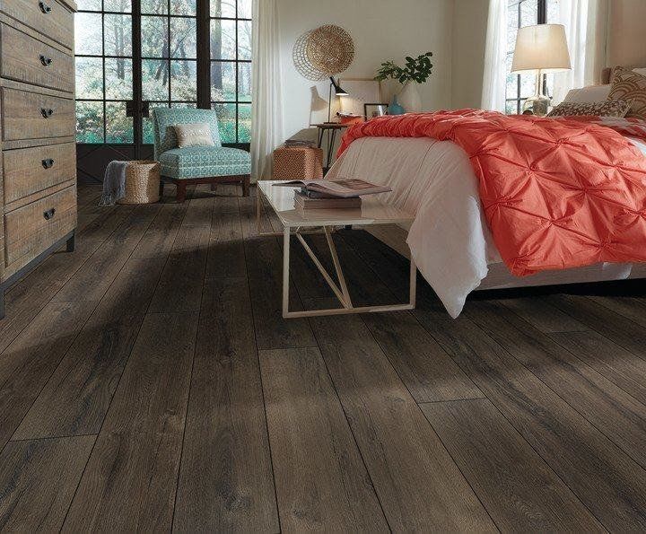 Cozy bedroom with dark wood floors, orange quilted bedspread, and large window letting in natural light