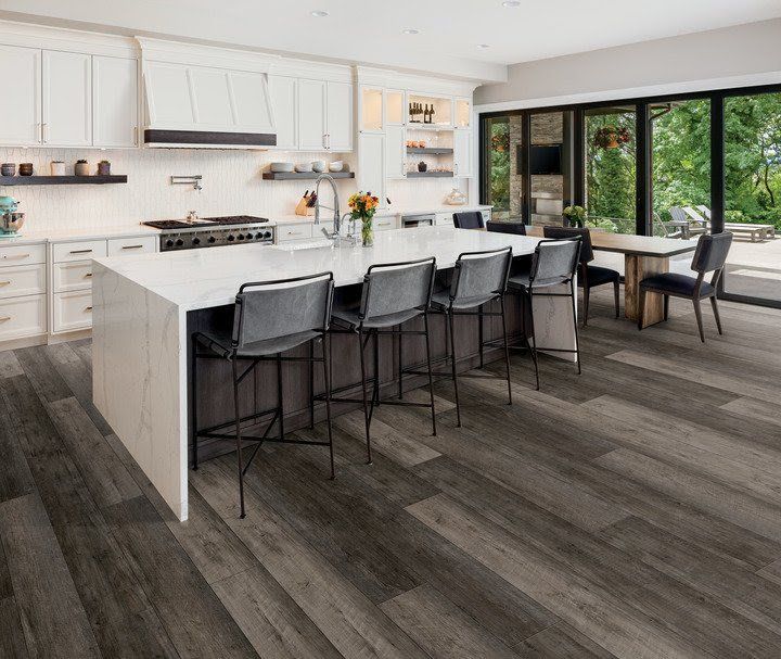 Modern white kitchen with large island, black barstools, and dining area by floor-to-ceiling windows.