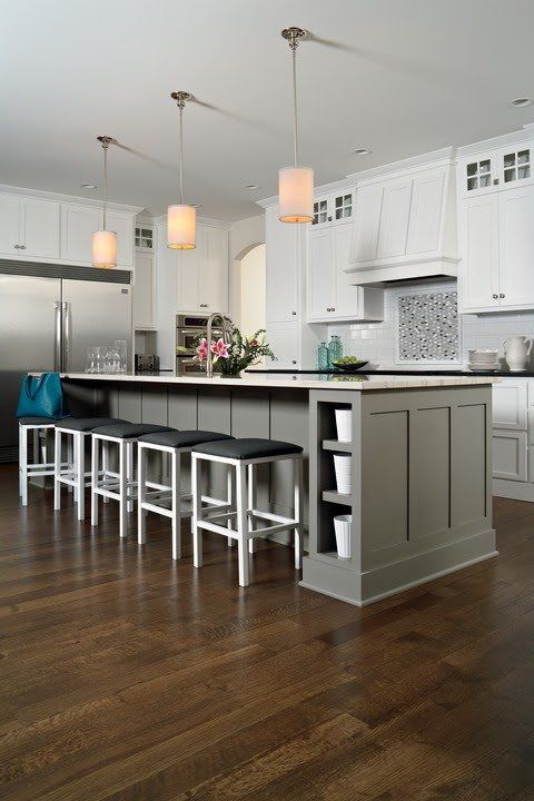 Modern kitchen with white cabinets, gray island, bar stools, pendant lights, and dark hardwood floors