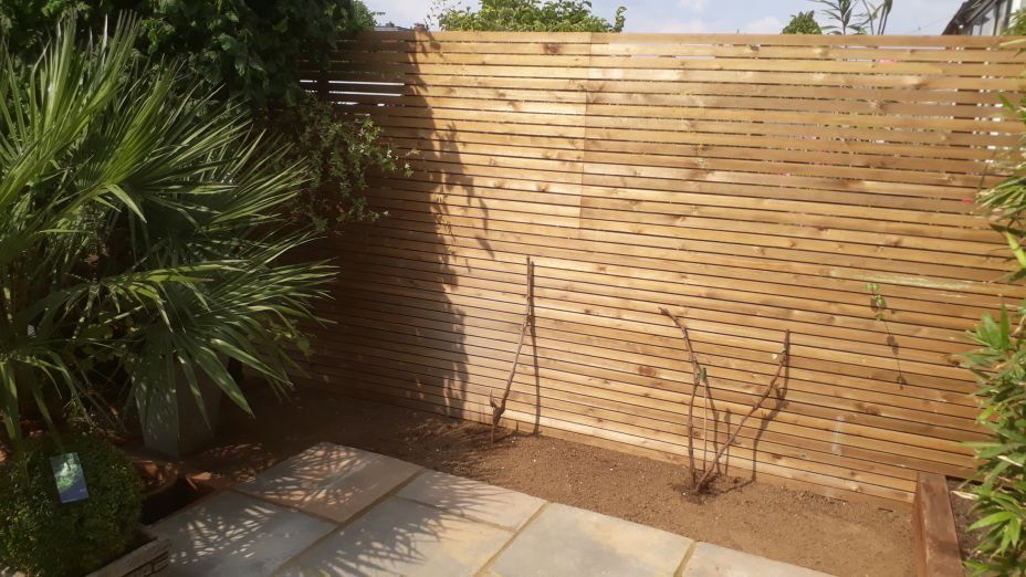 A wooden fence surrounds a patio in a garden.
