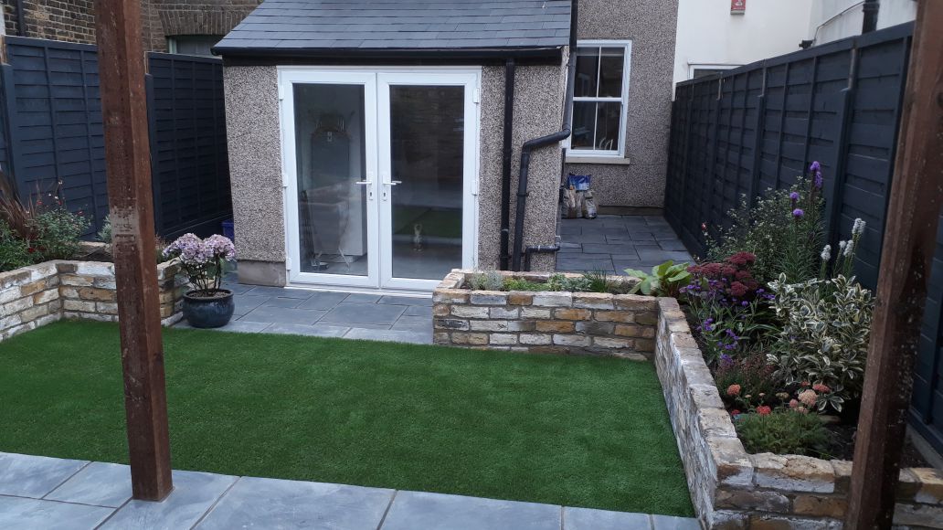 A small backyard with a house in the background and a lush green lawn.