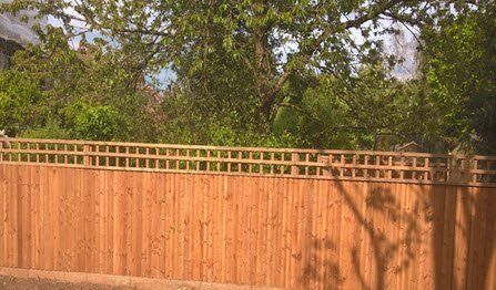 feather edge fencing installer A wooden fence with a trellis on top of it surrounded by trees.
