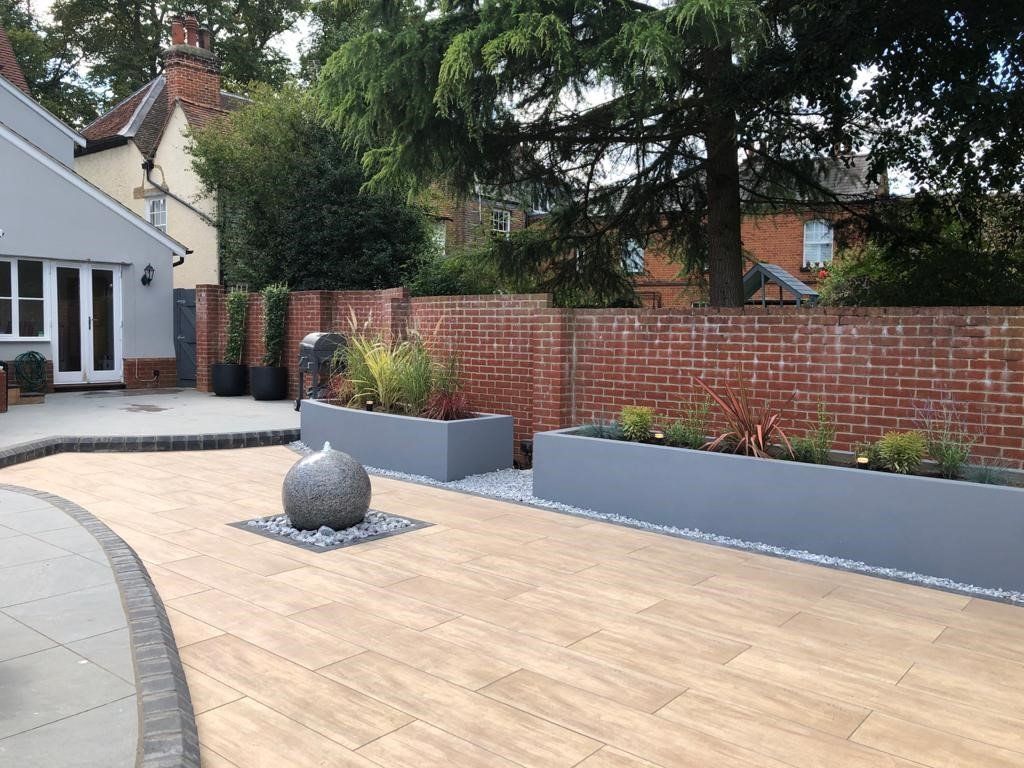 A brick wall surrounds a patio with planters and a fountain.
