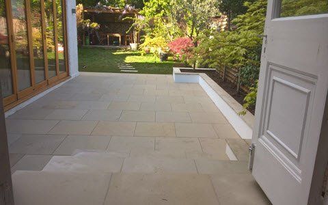 A white door is open to a patio with a garden in the background.