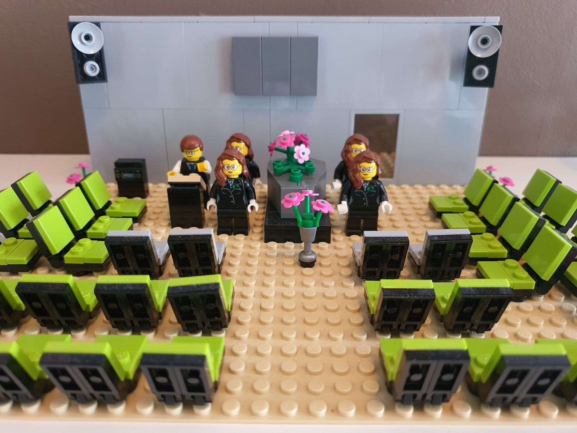 Een Lego-model van een formele bijeenkomst in een auditorium met figuren in pakken, limoengroene stoelen en bloemstukken.
