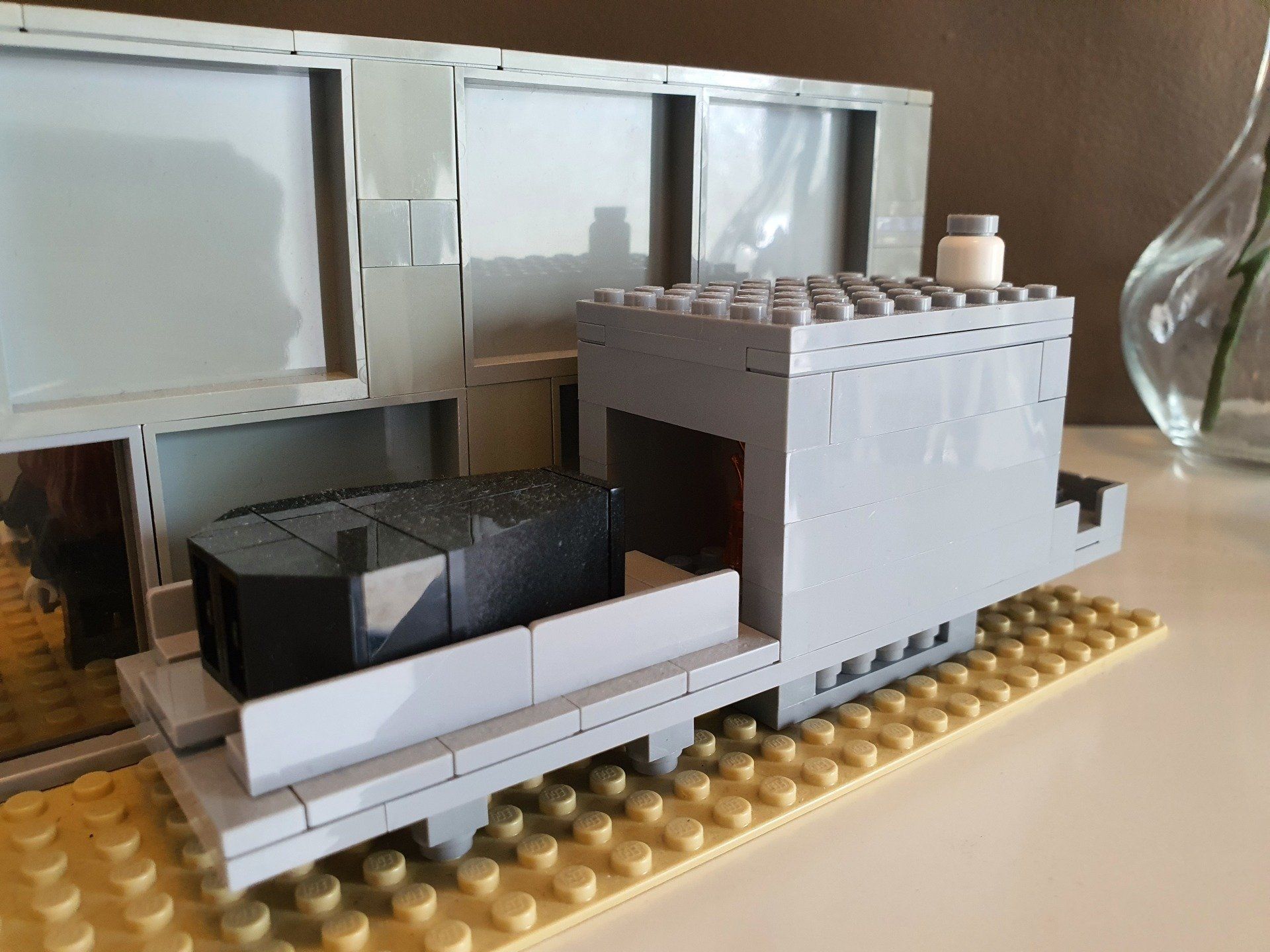 Een grijs LEGO-treinmodel staat op een gele grondplaat naast een spiegelend oppervlak.