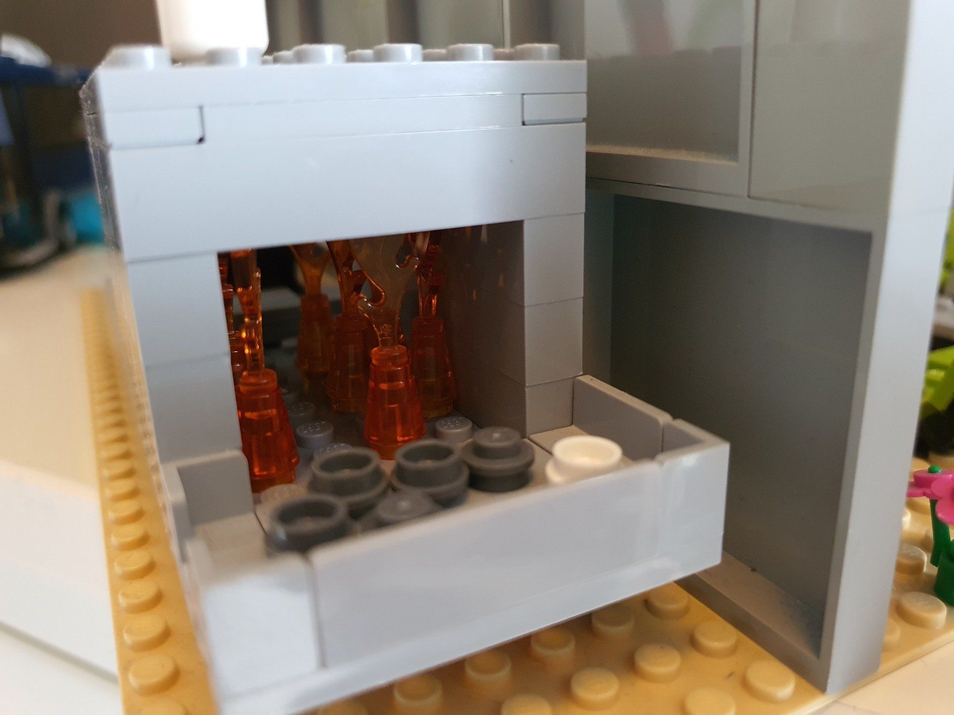 Een grijze Lego-structuur met een holle binnenkant gevuld met oranje, doorschijnende stukjes, die op een beige grondplaat staat.