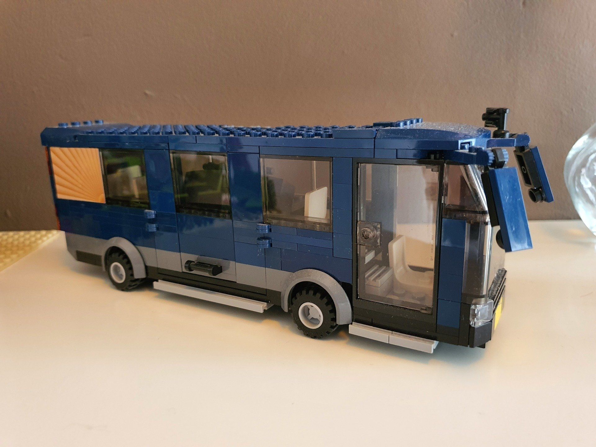 Een blauw-grijs LEGO-busmodel staat op een witte tafel.
