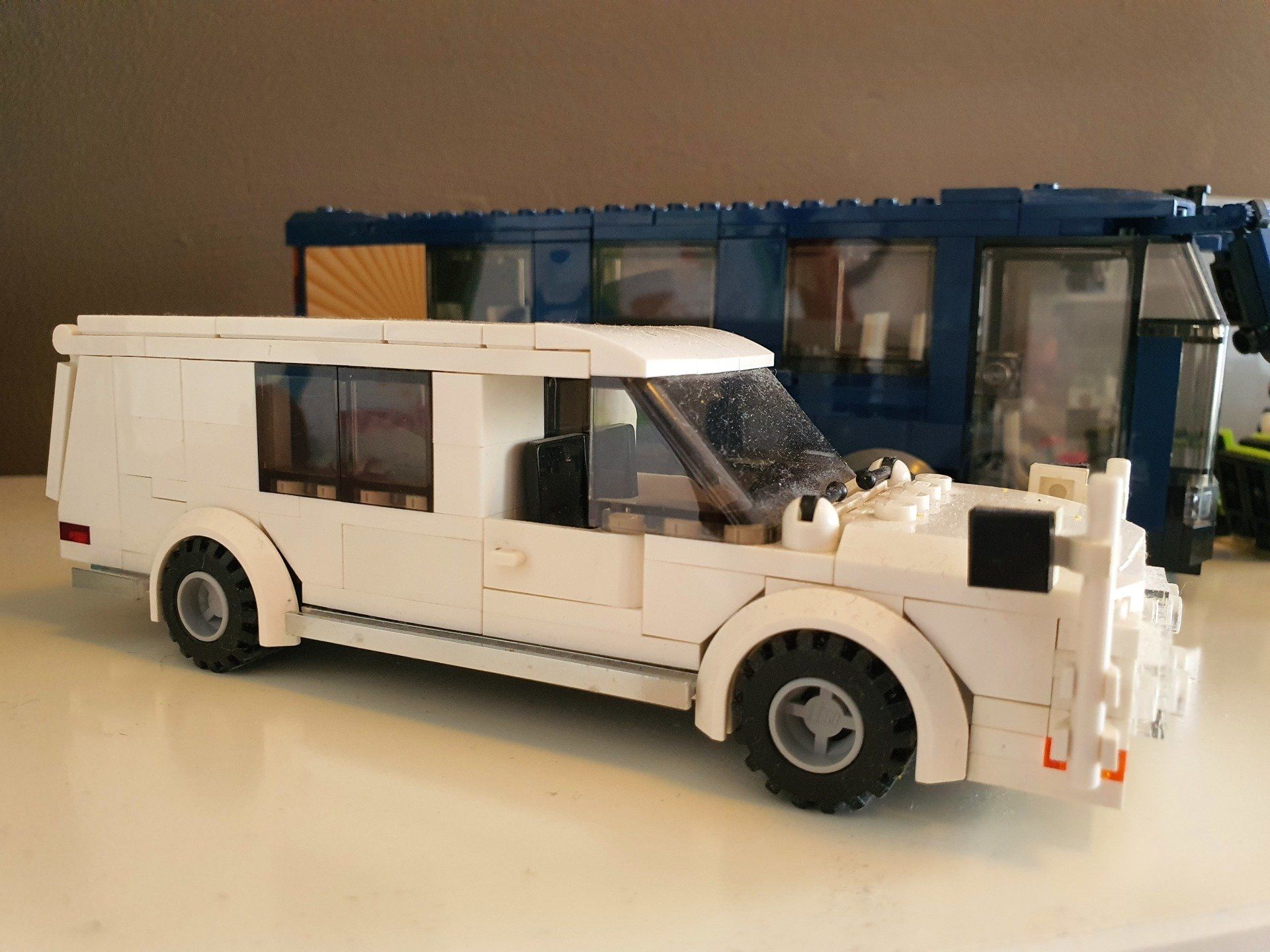 Een witte LEGO-lijkwagen staat geparkeerd voor een blauwe LEGO-bus op een vlakke ondergrond.