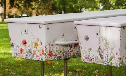 Twee witte, met bloemenmotief versierde doodskisten staan op sokkels in een grasrijke buitenomgeving.