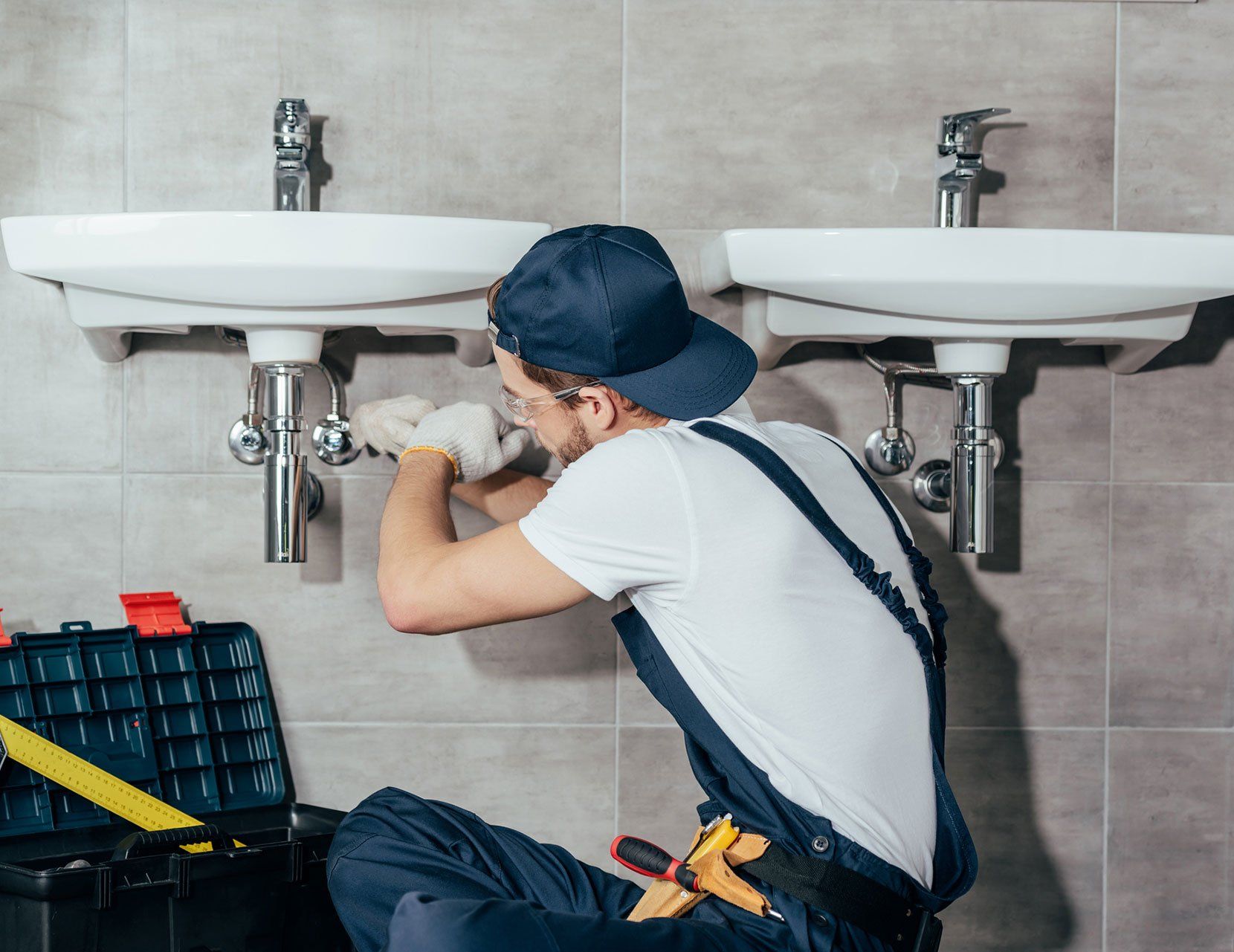 Back view of young professional plumber fixing sink in bathroom