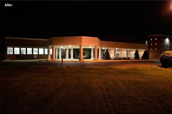 Night view of a well-lit beige building with columns. The setting is dark, with a grassy lawn.