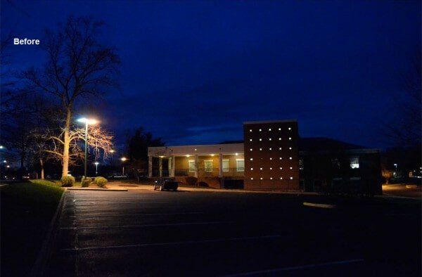 Nighttime exterior view of a building with a brick facade and a parking lot. Blue sky and street lights.