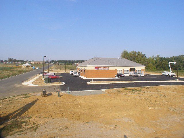 Bank building, brick with dark asphalt. Sunny day, construction equipment nearby. Road and undeveloped land.