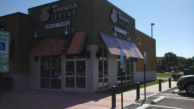Exterior of a Panera Bread restaurant with awnings, windows, and a parking area on a sunny day.