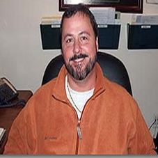 Jessie Fizer - recessed lighting in Fredericksburg, VA Man with beard smiles, seated at a desk. Wearing orange Columbia jacket and white undershirt. Office setting.