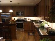 Wooden kitchen with stainless steel appliances, dark countertops, and hanging pendant lights.