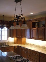 Kitchen with brown cabinets, granite countertops, chandelier, and under-cabinet lighting.
