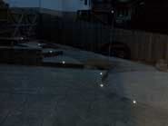 Dark outdoor scene with lit ground lights leading up to steps near a wooden fence.