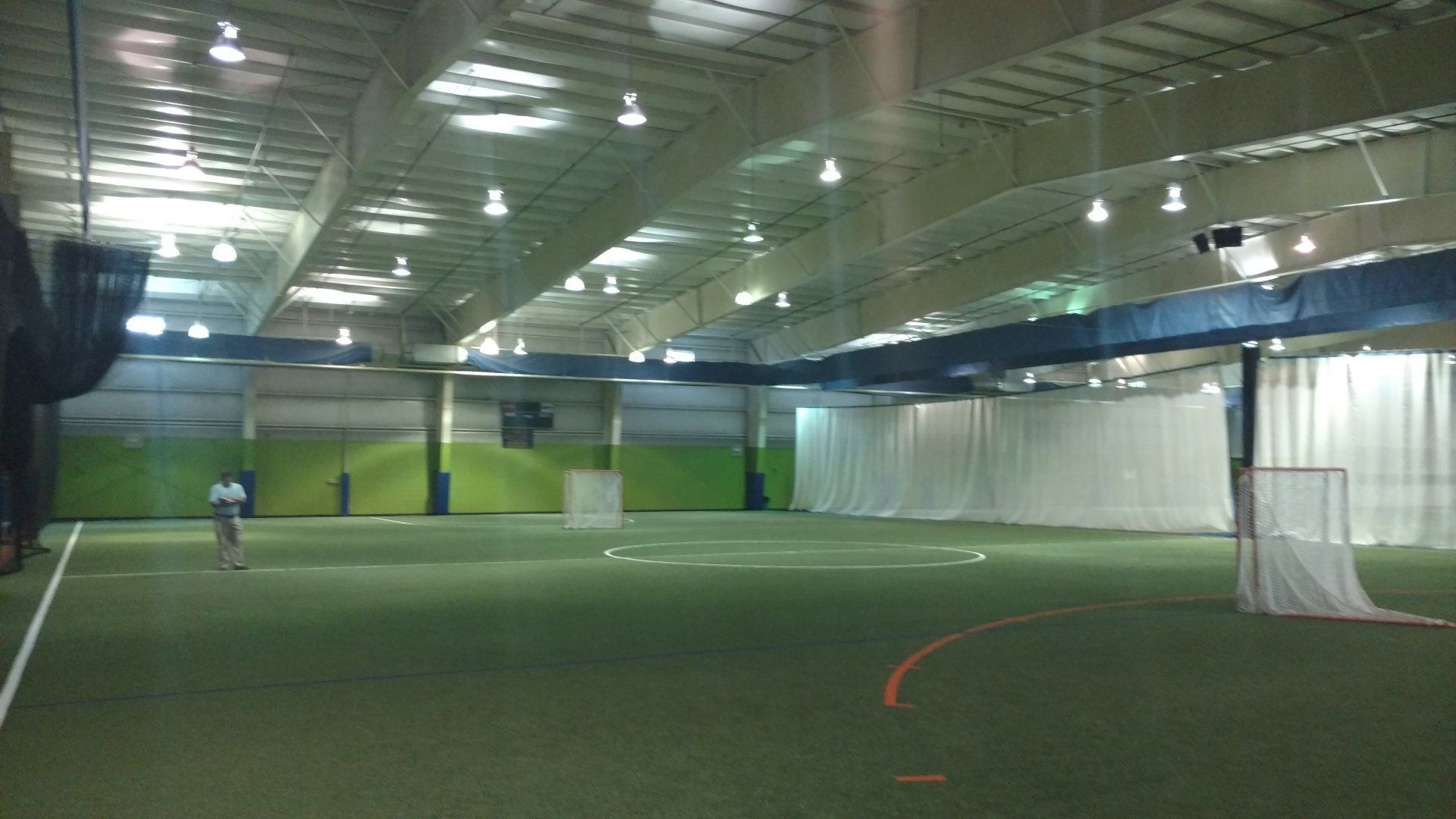 Indoor sports field with artificial turf, lacrosse goal, and a person practicing.