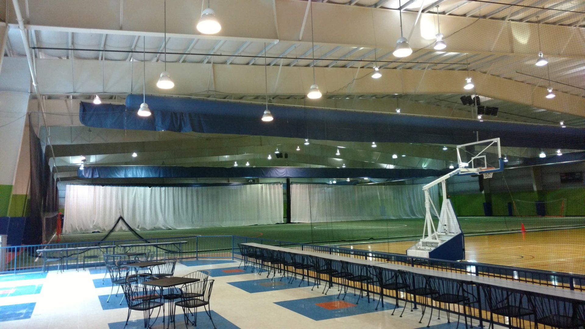 Indoor sports complex with basketball court, tables, and hanging lights.