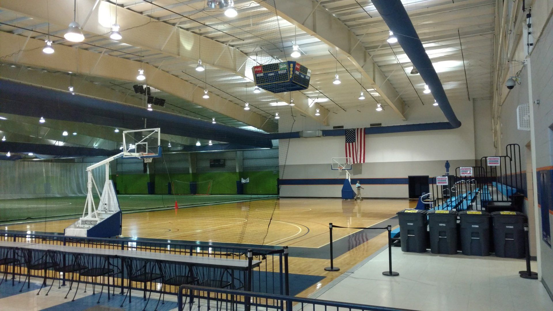 Indoor basketball court with a wooden floor, a scoreboard, and an American flag.