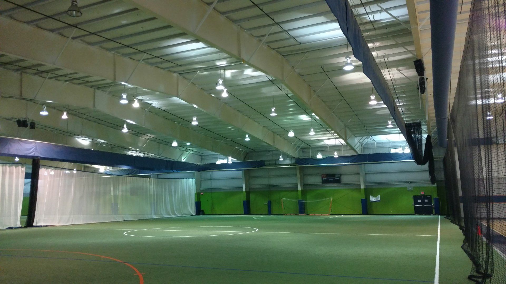 Indoor sports facility with green field, white walls, blue accents, and hanging lights.