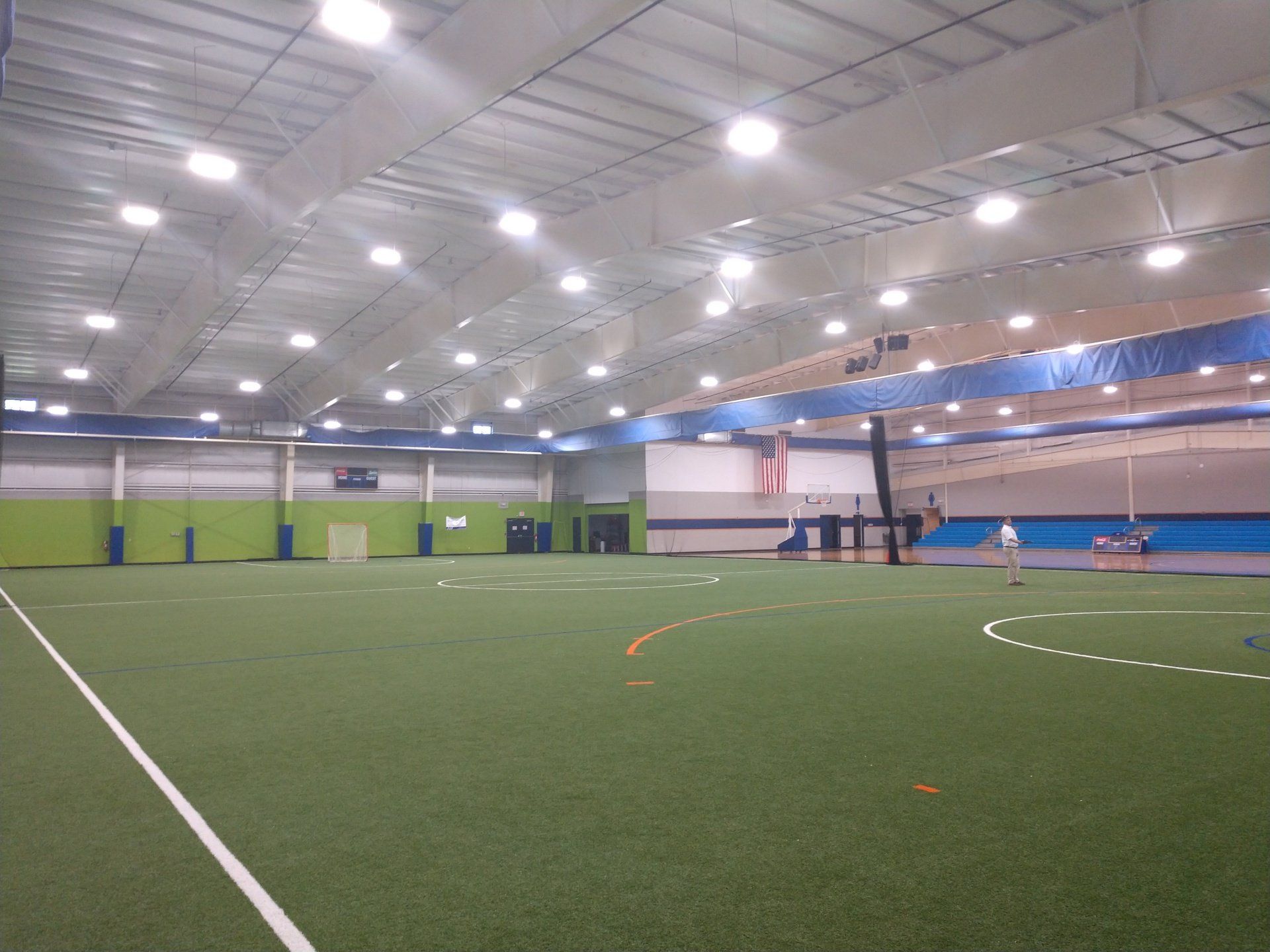 Indoor sports arena with green turf field, blue walls, and bright overhead lights.