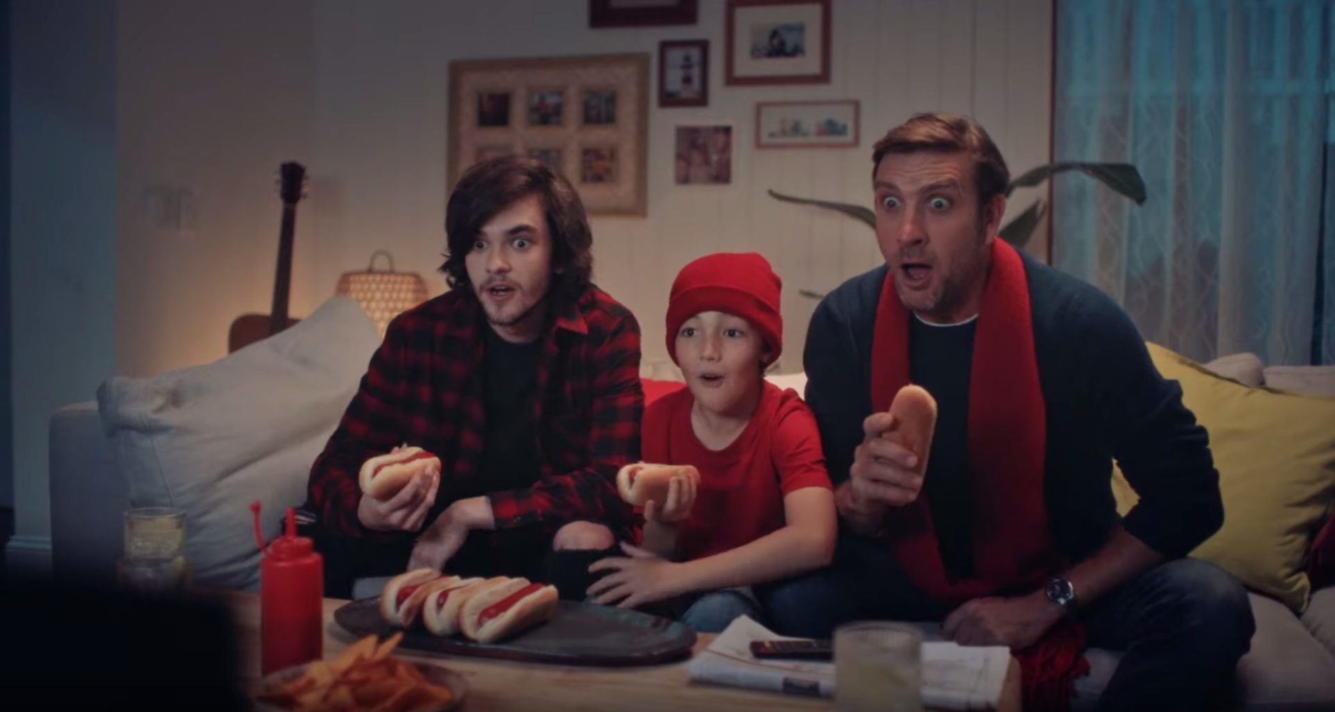 A family sat on a couch eating food and watching sports on the TV