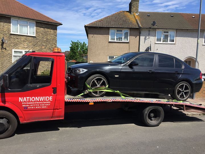 A.C Recovery's, 24 hour towing service in Barking and Dagenham, black car being towed by a red towing truck in broad daylight