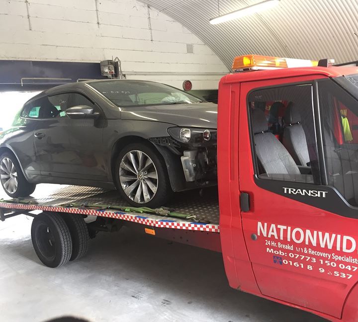 A.C Recovery's, 24 hour towing service in Barking and Dagenham, black wrecked car towed by red towing truck and brought inside the repair centre