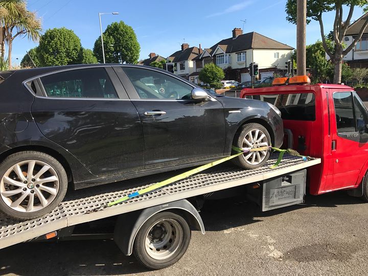 A.C Recovery's, 24 hour towing service in Barking and Dagenham, black car being towed by a red towing truck in the morning