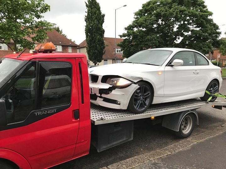 A.C Recovery's, 24 hour towing service in Barking and Dagenham, white wrecked car being towed by a red towing truck in the afternoon