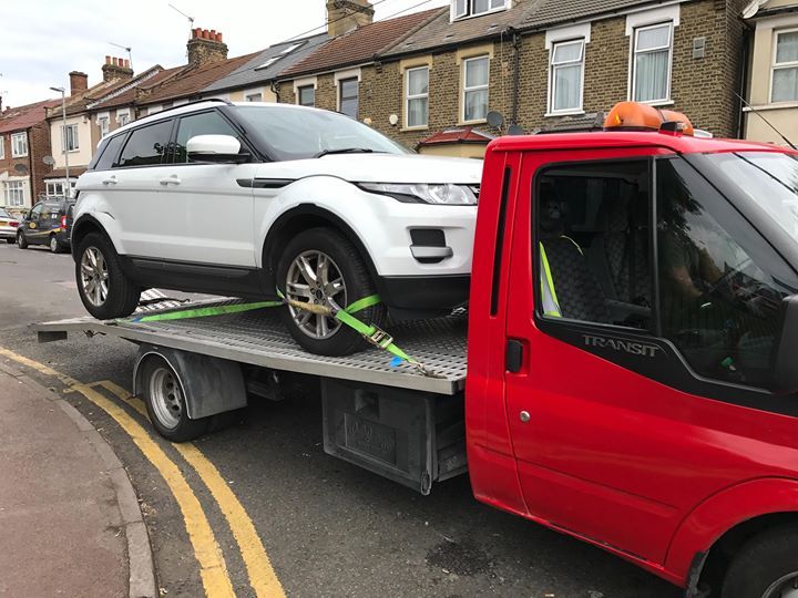 A.C Recovery's, 24 hour towing service in Barking and Dagenham, white SUV being towed by red towing truck in the afternoon