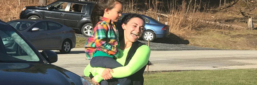 smiling mom carrying preschool aged child outdoors near a road