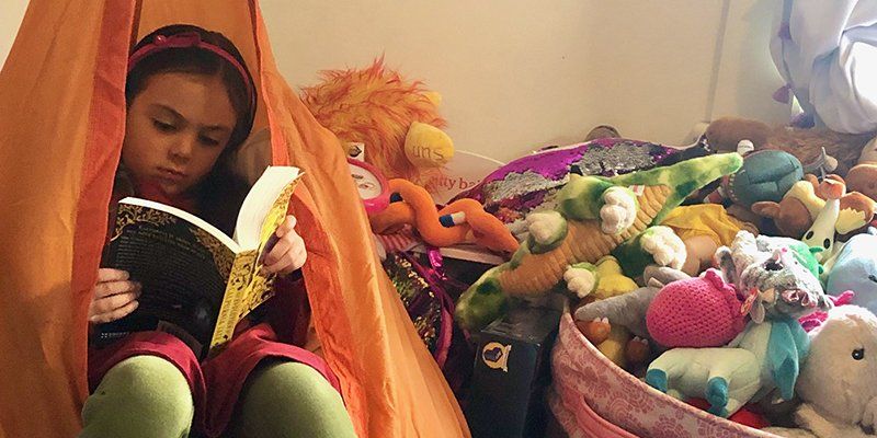 child reading in a hanging pod chair, surrounded by stuffed animals