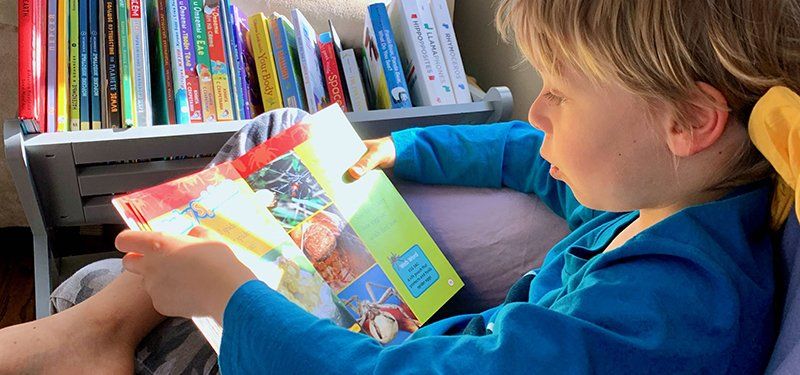 boy reading book in small chair next to book shelf