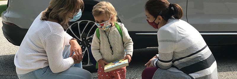 child with two crouching adults in front of car