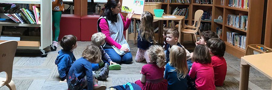 Guide sitting on the floor with a circle of preschool aged children, reading a book